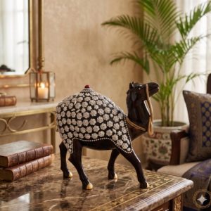 Handcrafted dark wood camel statue with silver floral metal embossing on a luxury marble table.